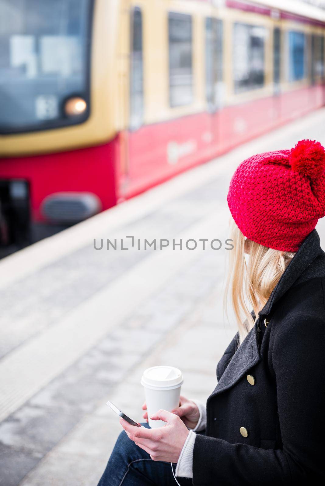 Woman waiting for suburban train in station drinking coffee holding a phone