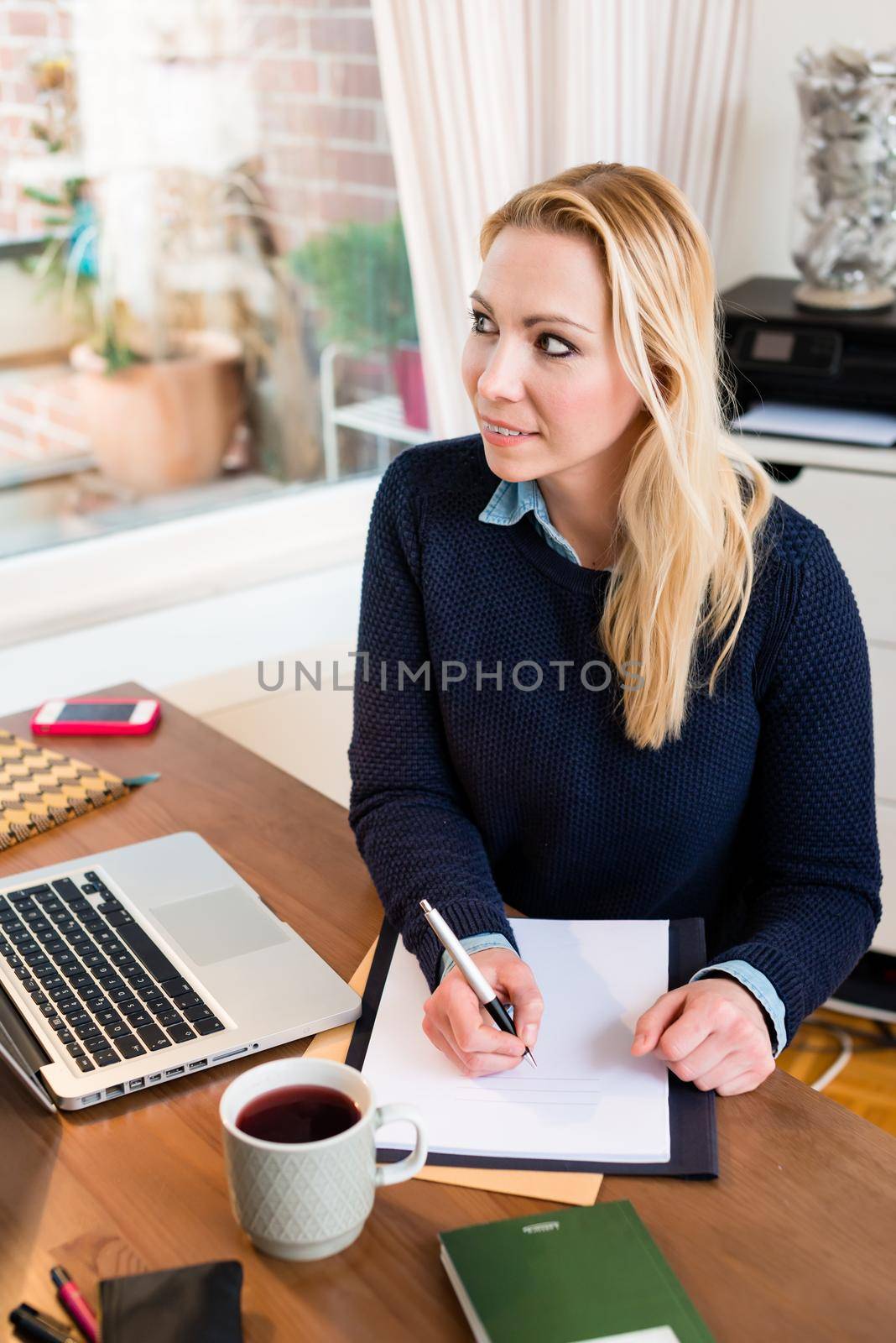 Portrait of a contemplating woman at her desk writing on paper
