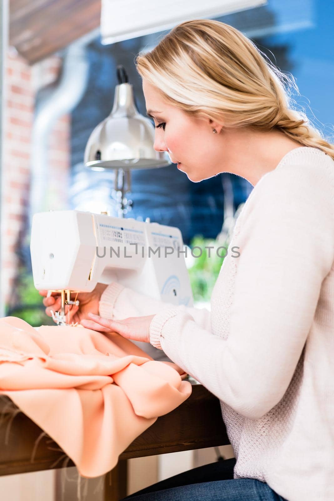 Woman stitching clothes on sewing machine by Kzenon