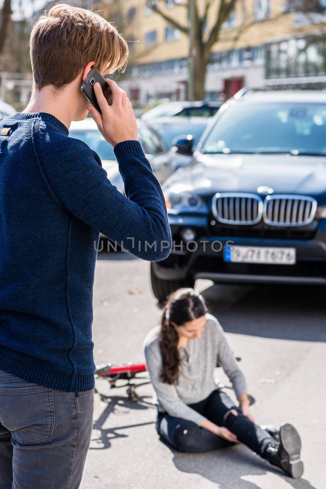Full length view of a worried young driver calling the ambulance after hitting and injuring accidentally a female bicyclist on a city street