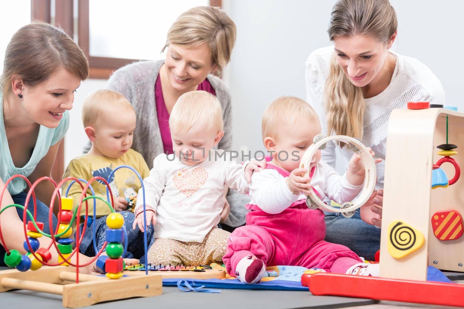 Three happy mothers watching their babies playing with safe multicolored toys by Kzenon