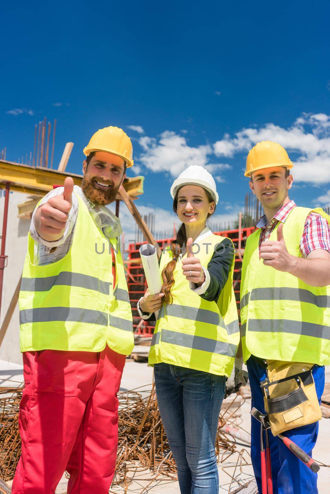 Three colleagues in a construction team showing thumbs up during work by Kzenon