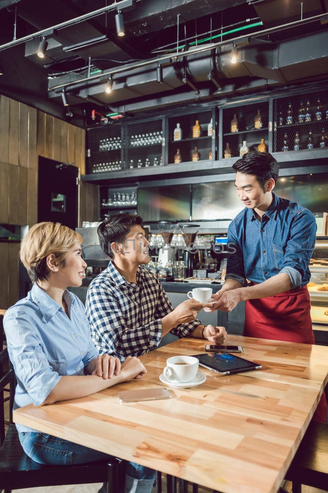 Waiter serving coffee to the young couple sitting in the cafe