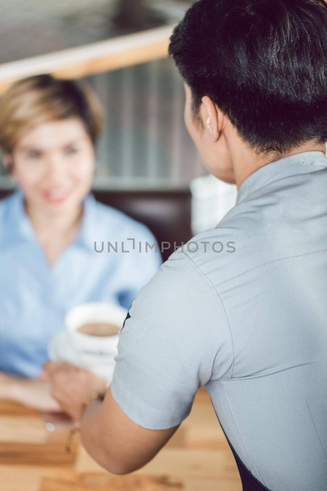 Rear view of male waiter serving coffee to female customer