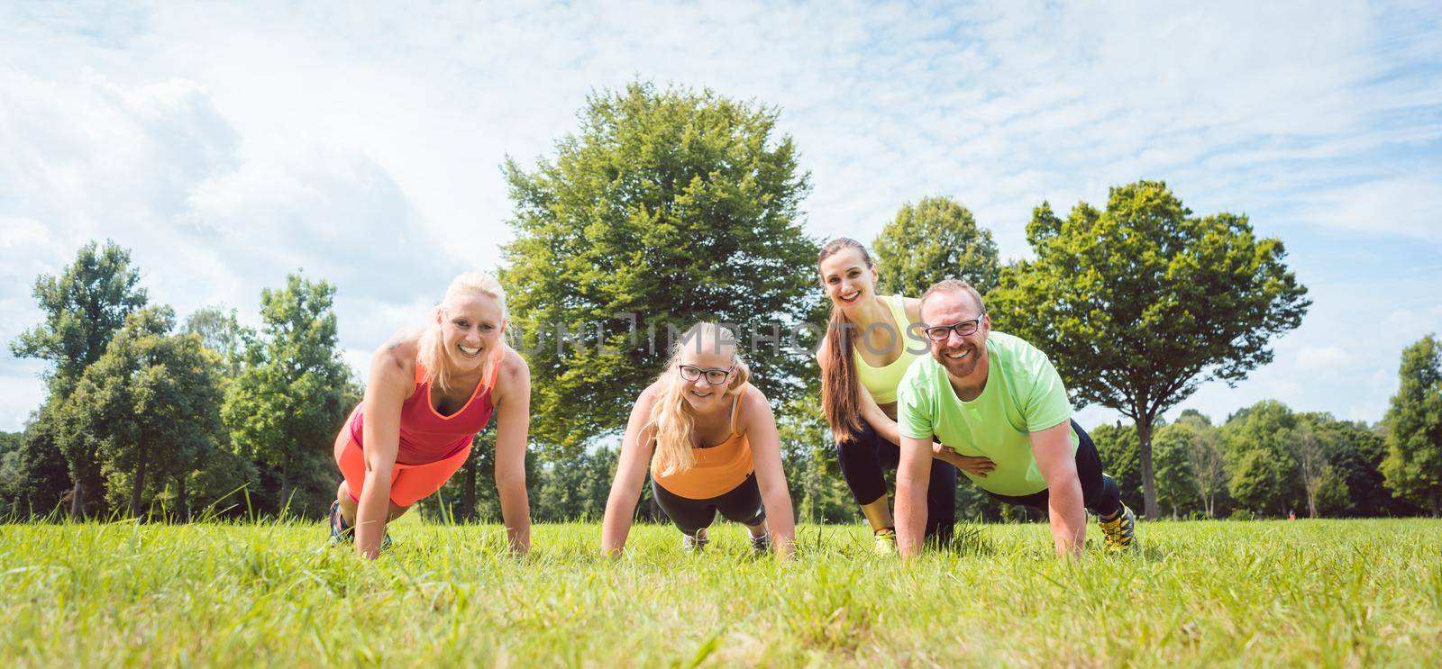 Family doing push-ups in nature under guidance by a fitness coac by Kzenon