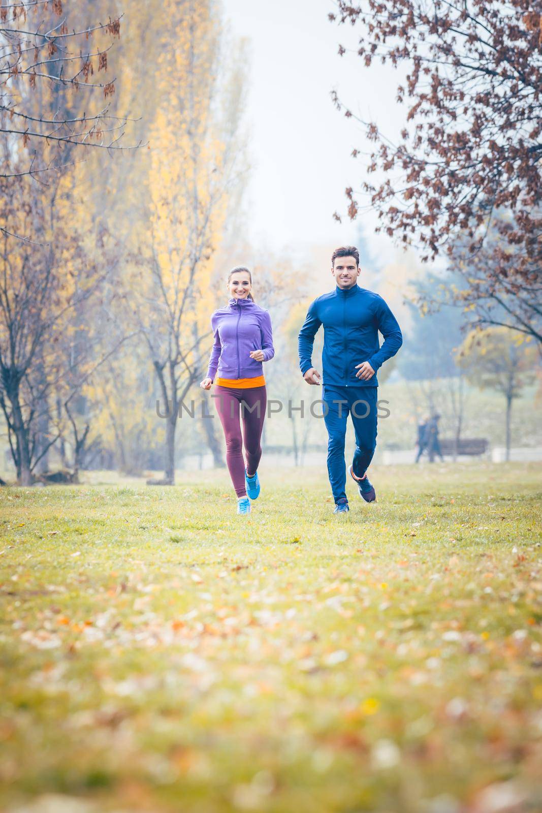 Woman and man running in autumn park for sport by Kzenon