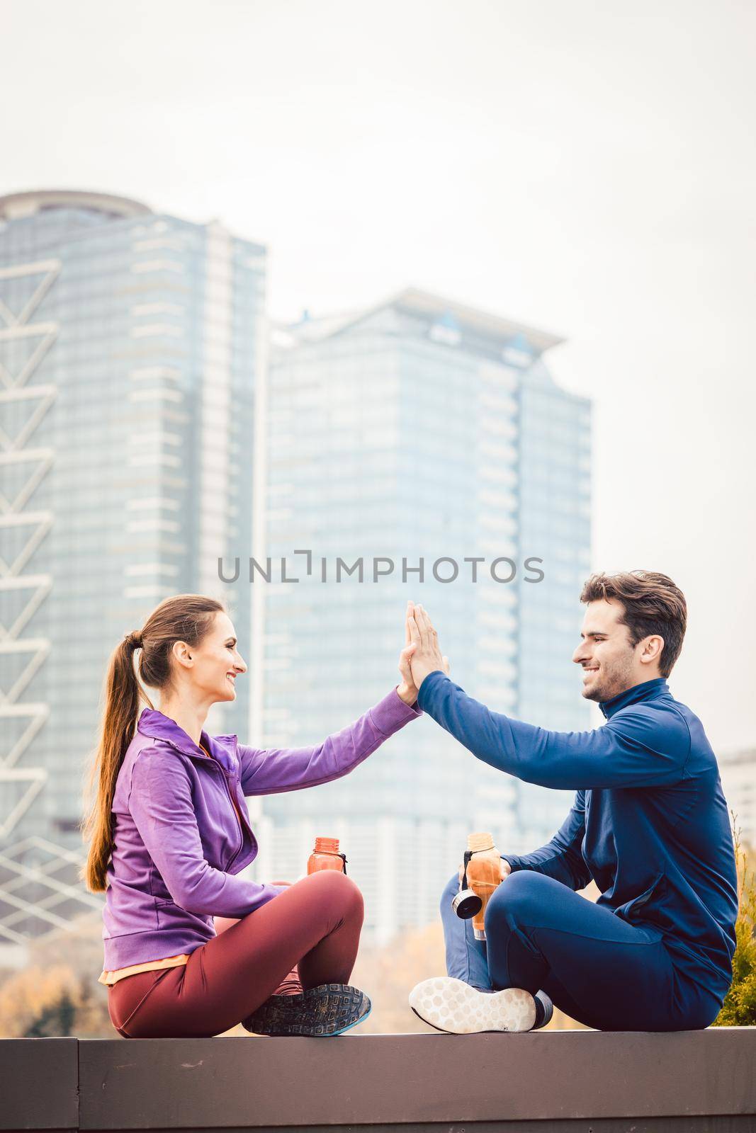 Woman and man giving hi-five after fitness sport in a city, in the background a high-rise building is to be seen