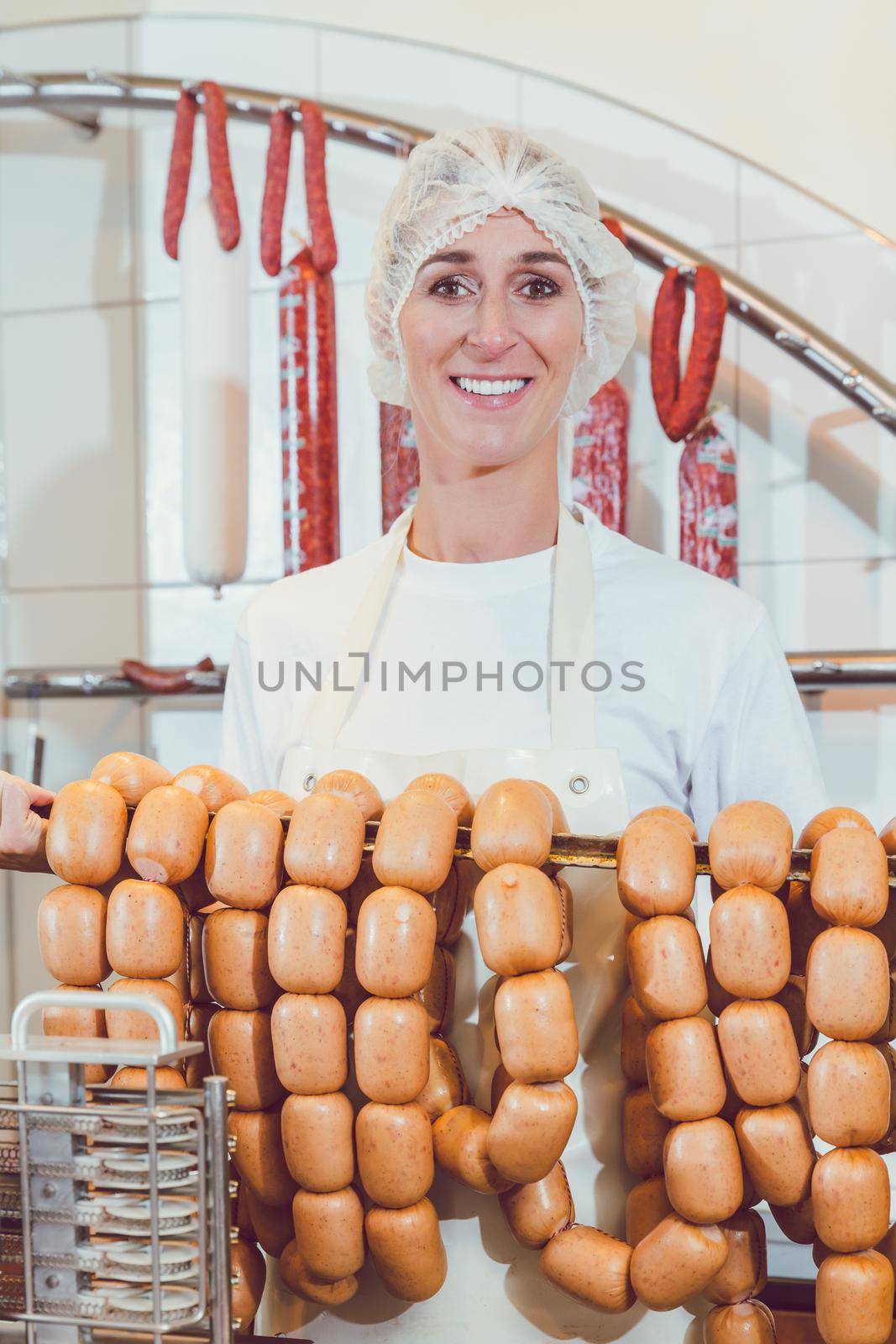Proud butcher woman showing sausages on a rail