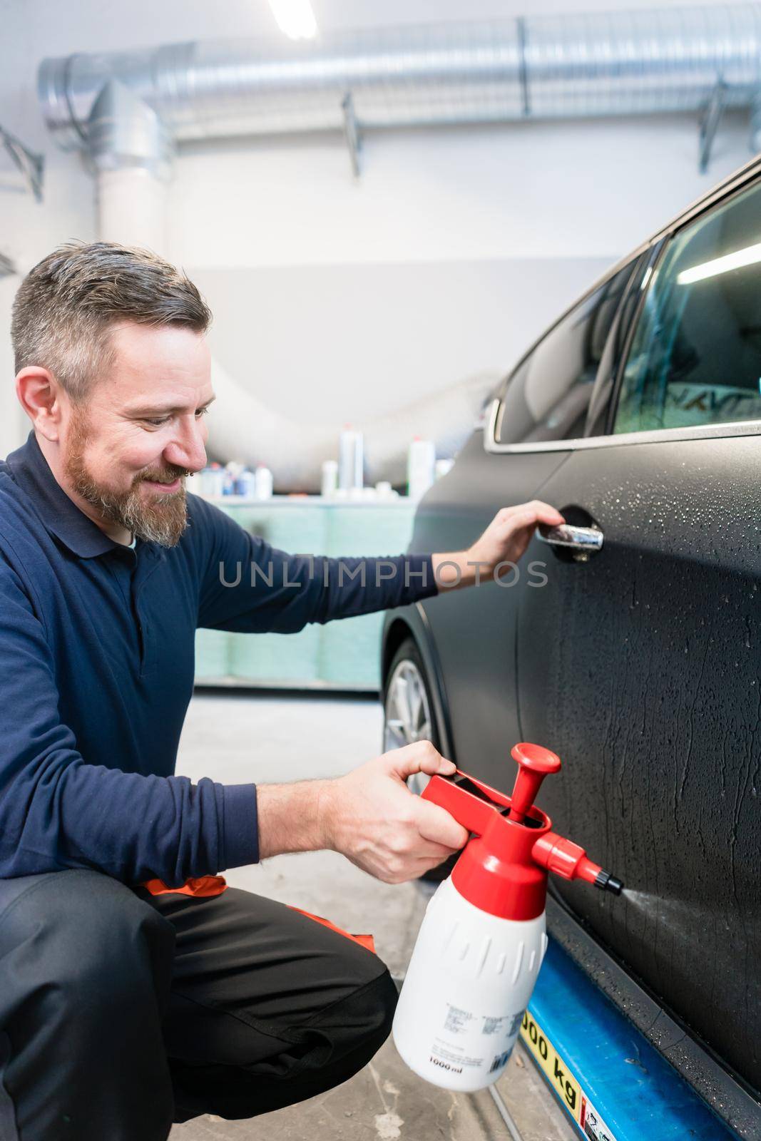 Man preparing car for putting advertisement sticker on it spraying water on the door