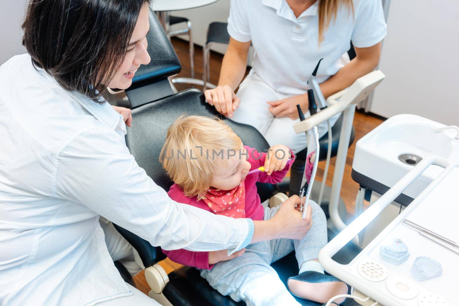 Woman dentist looking after baby teeth of a little girl by Kzenon