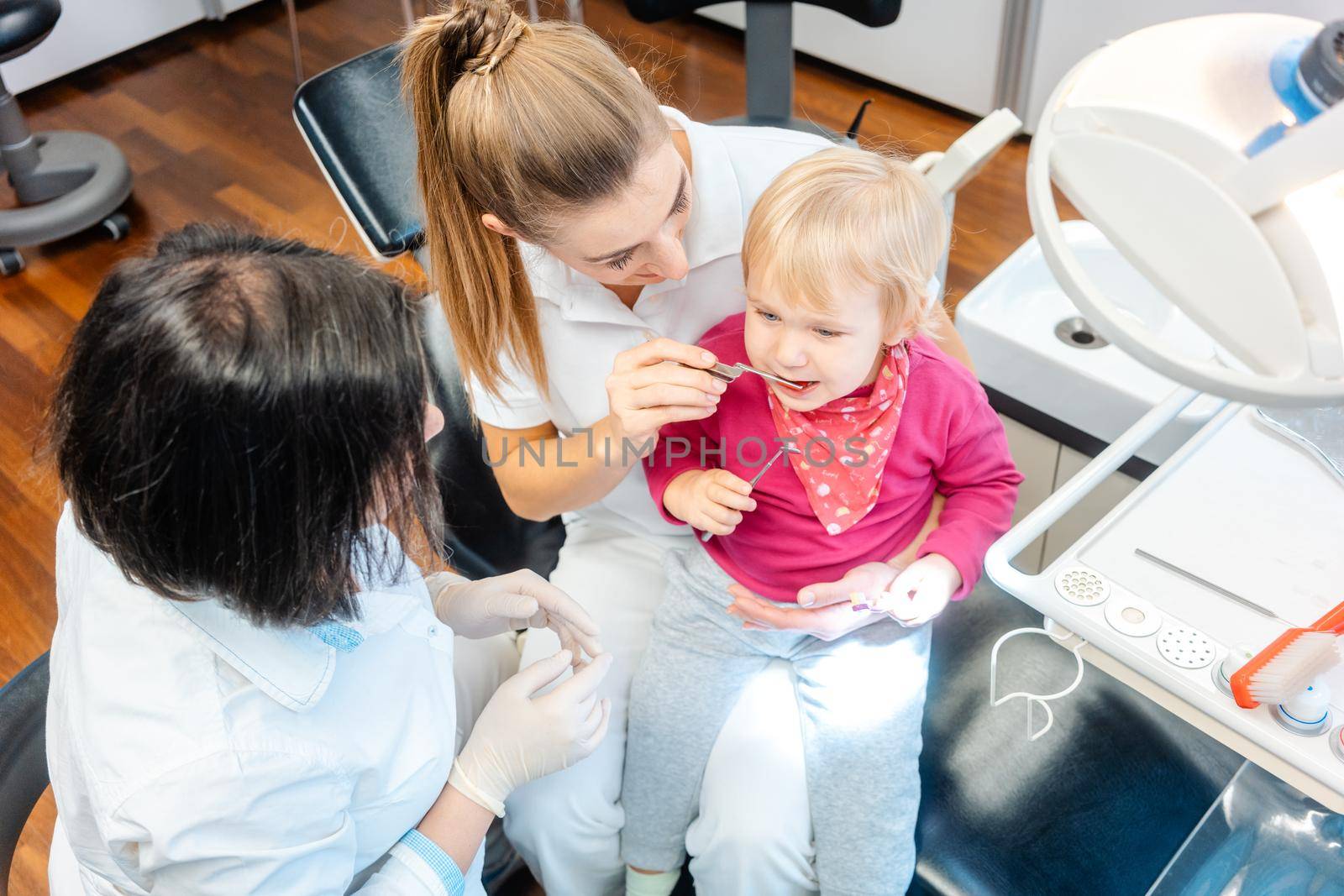 Woman dentist looking after baby teeth of a little girl by Kzenon