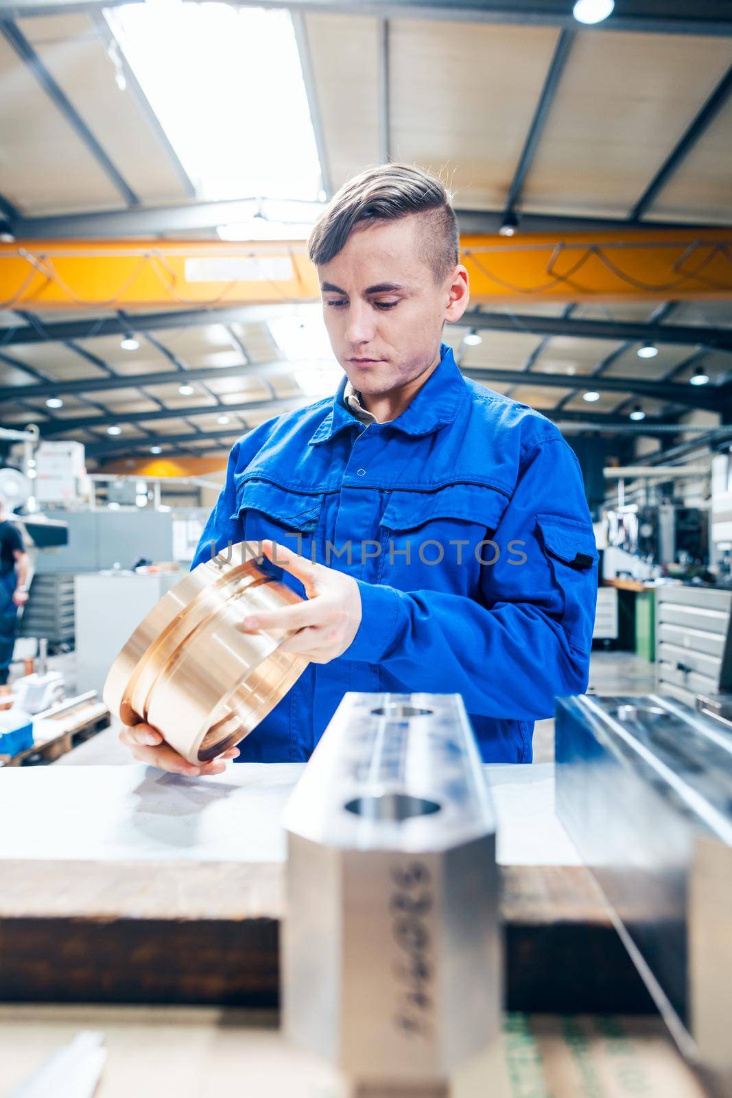 Apprentice in metalworking looking at workpiece by Kzenon