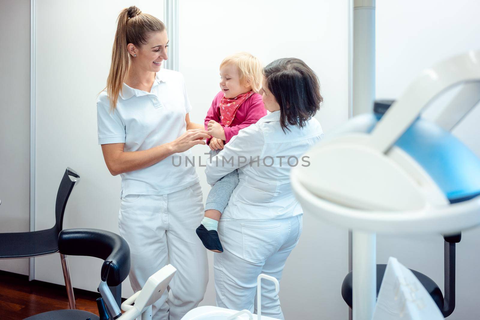 Dentist and her assistant with child in the office by Kzenon