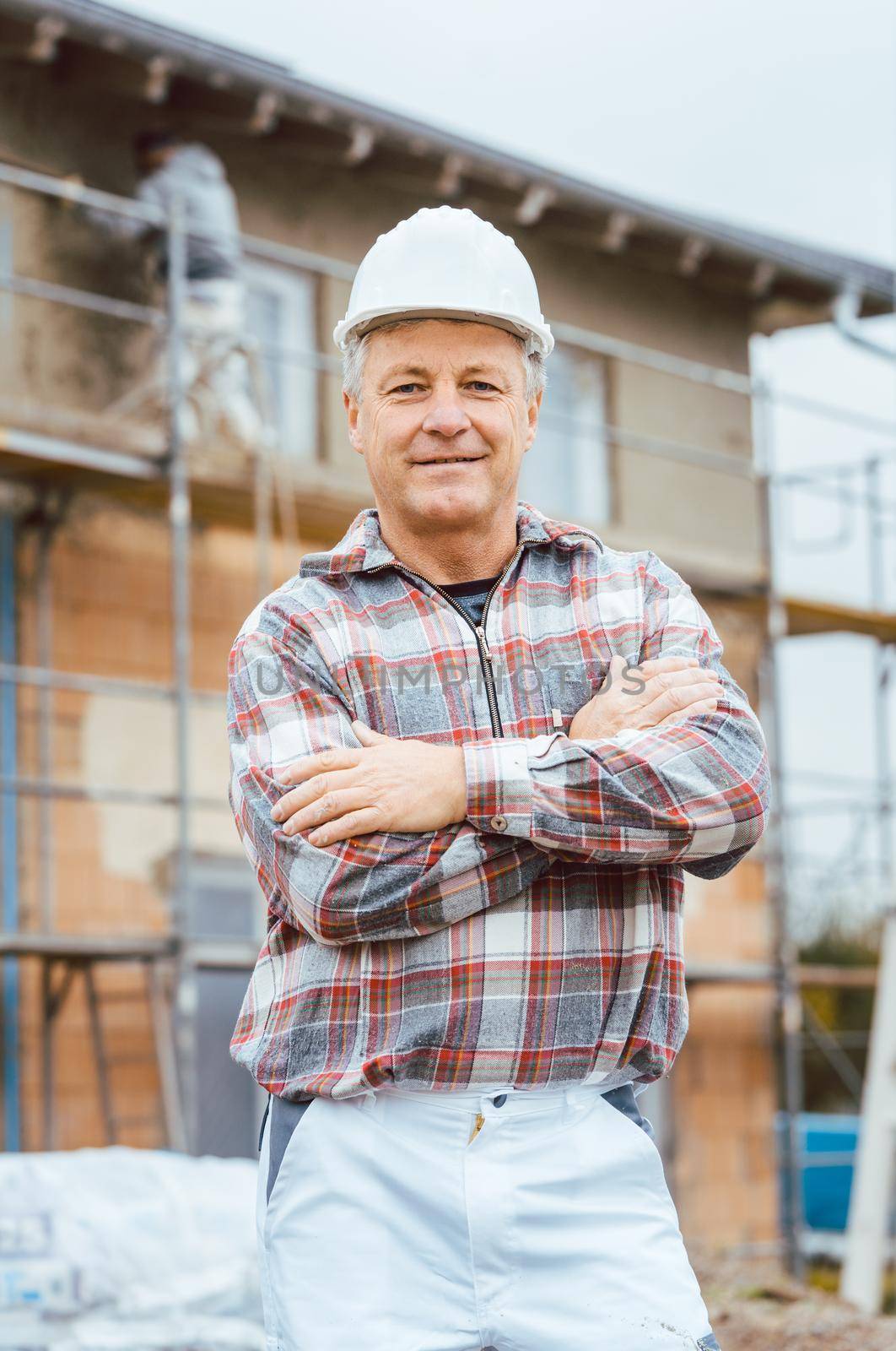 Proud plasterer standing in front of scaffold on construction site crossing arms