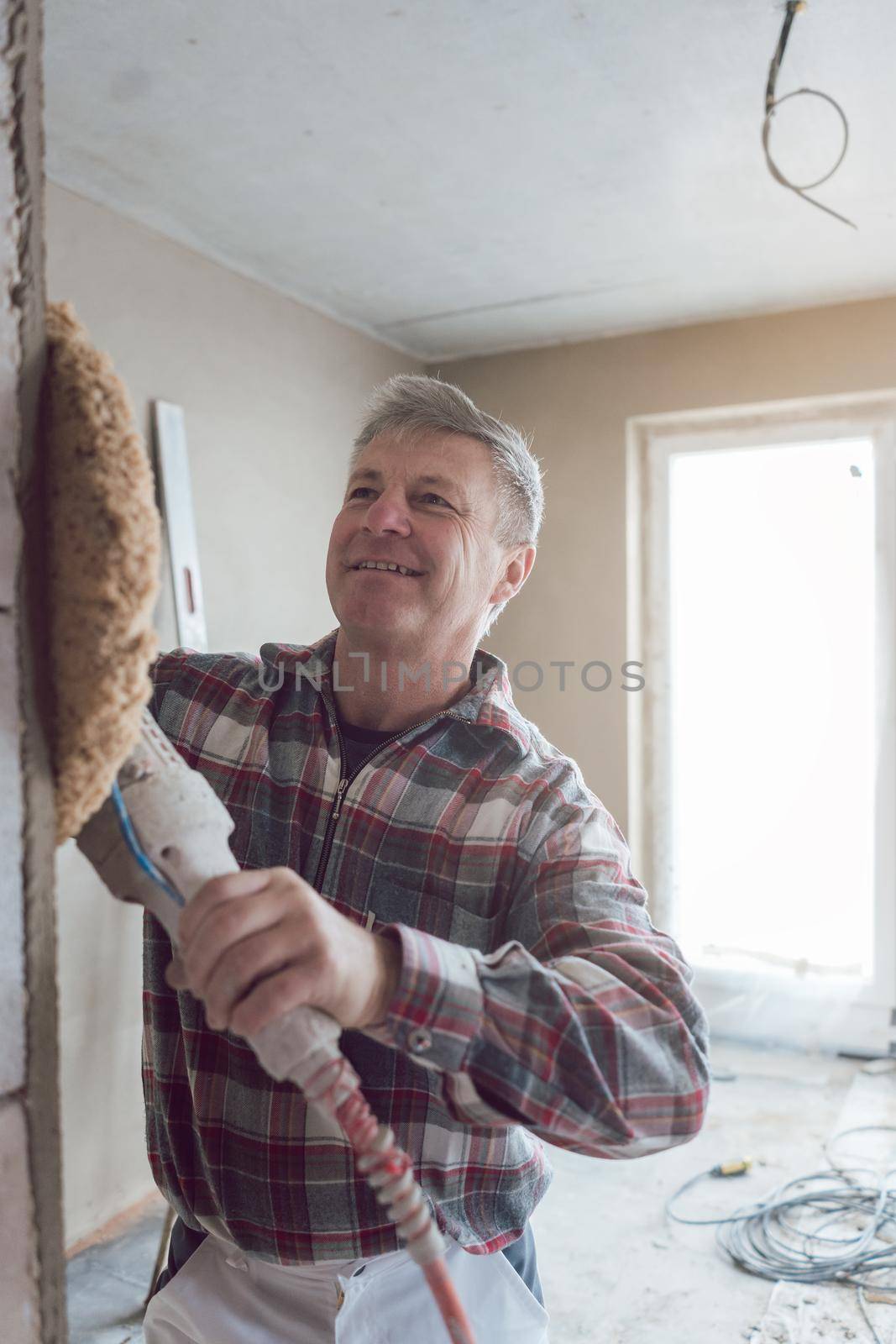 Plasterer man smoothing interior wall of new homes with machine