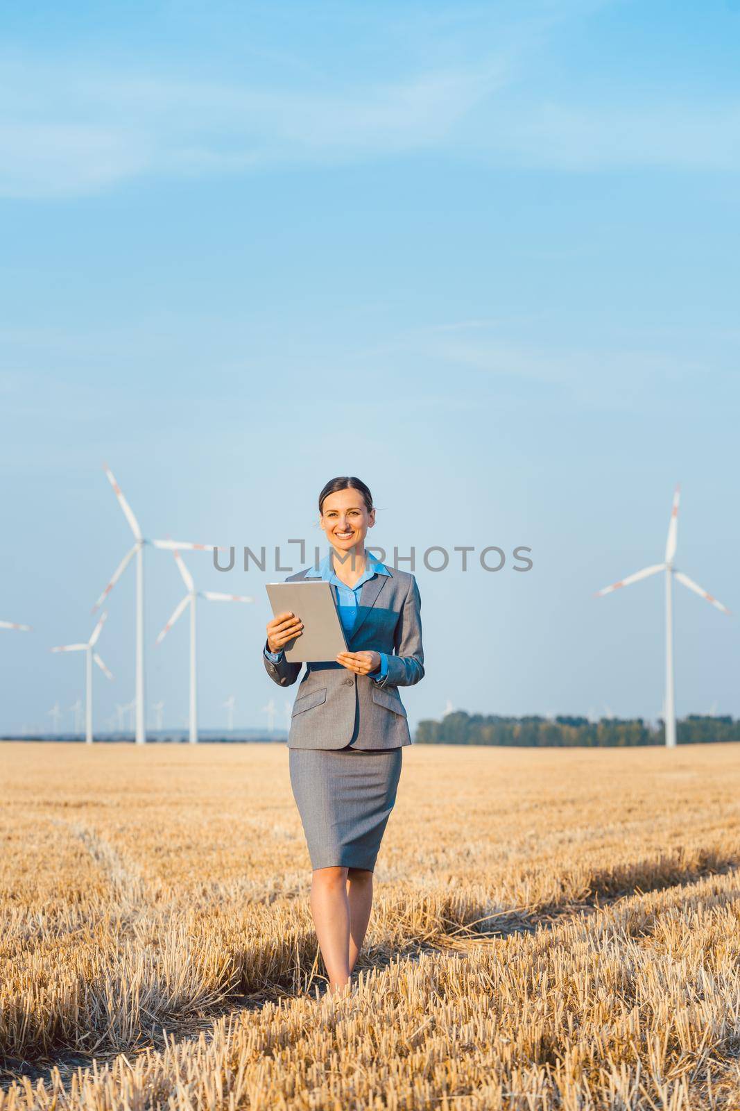 Women putting money into an ethical Investment of wind turbines, standing with her computer on a field