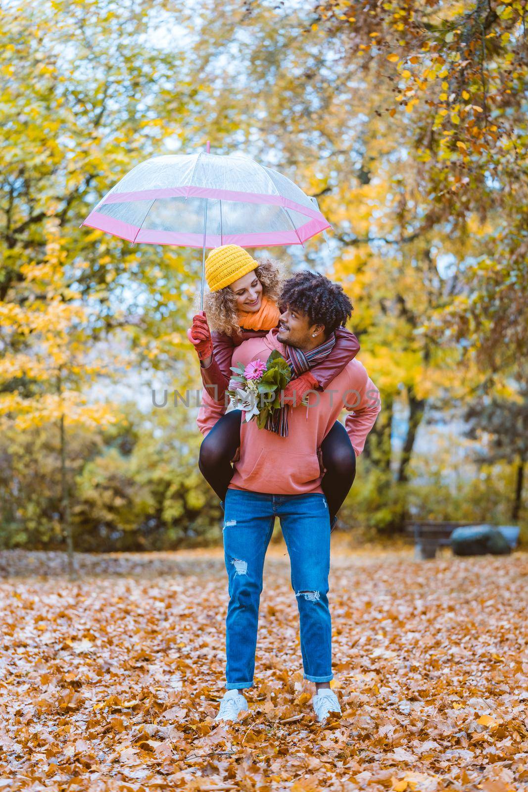 Black man carrying his Caucasian girl piggyback in fall both being joyful