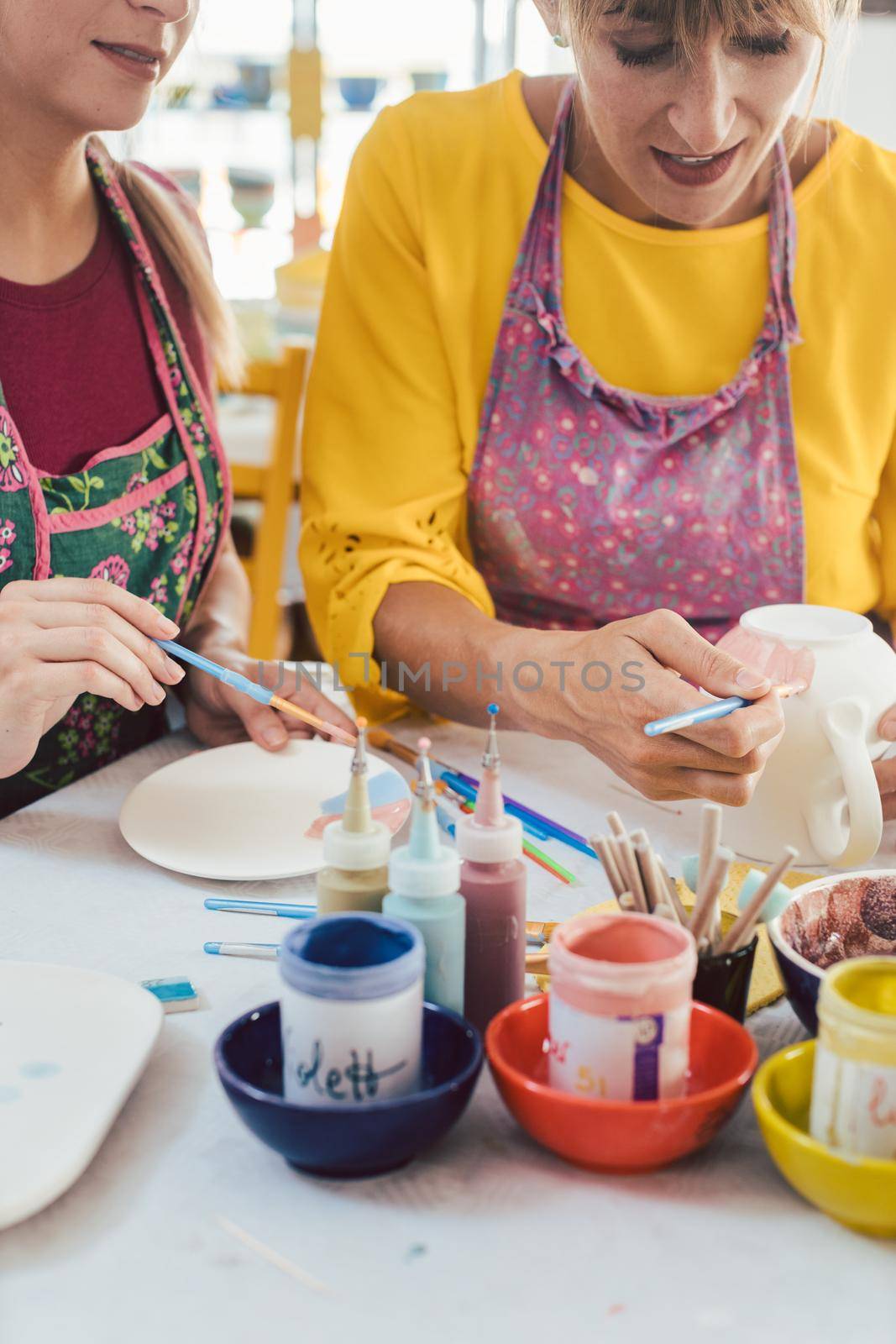 Two girl friends painting their own handmade ceramics in a hobby workshop