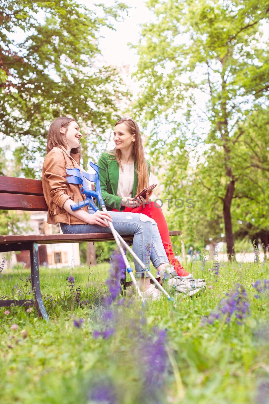 Two women, one healthy and one with a sprained foot, on a bench in the park