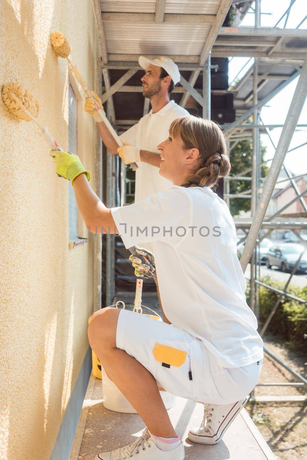 Woman painter painting a wall with yellow paint working hard