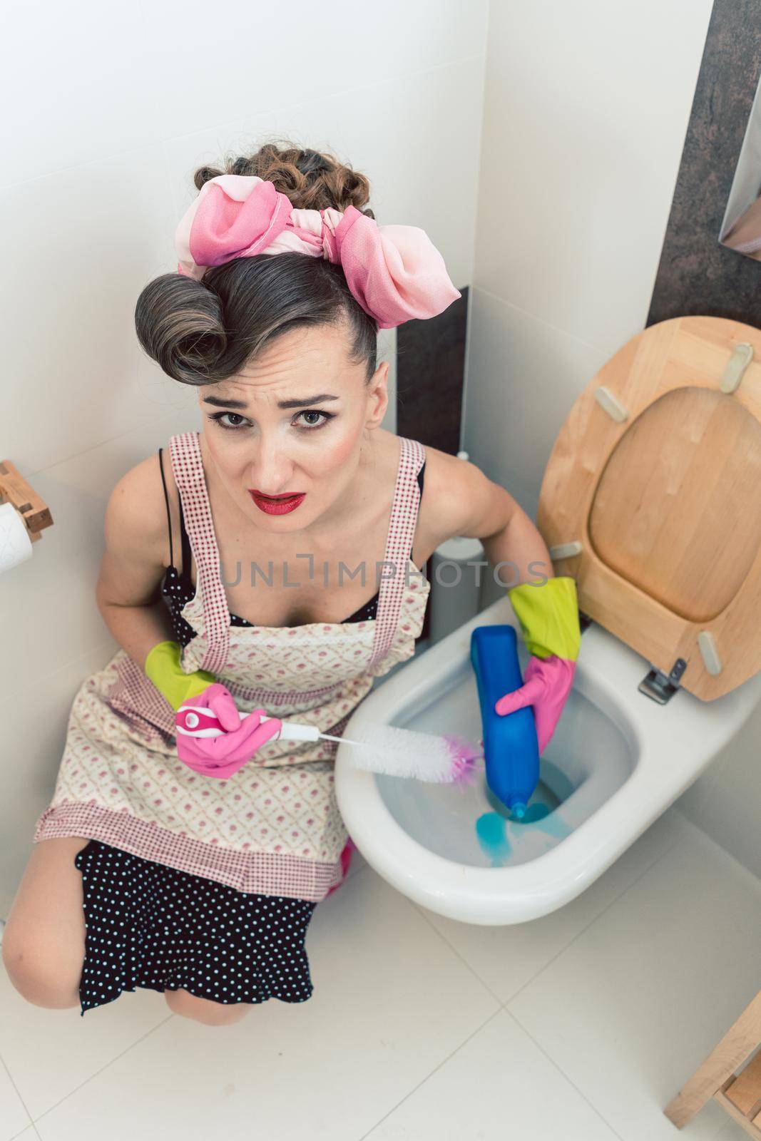 Homemaker having perfectly no fun at all cleaning the restroom with brush and household detergent