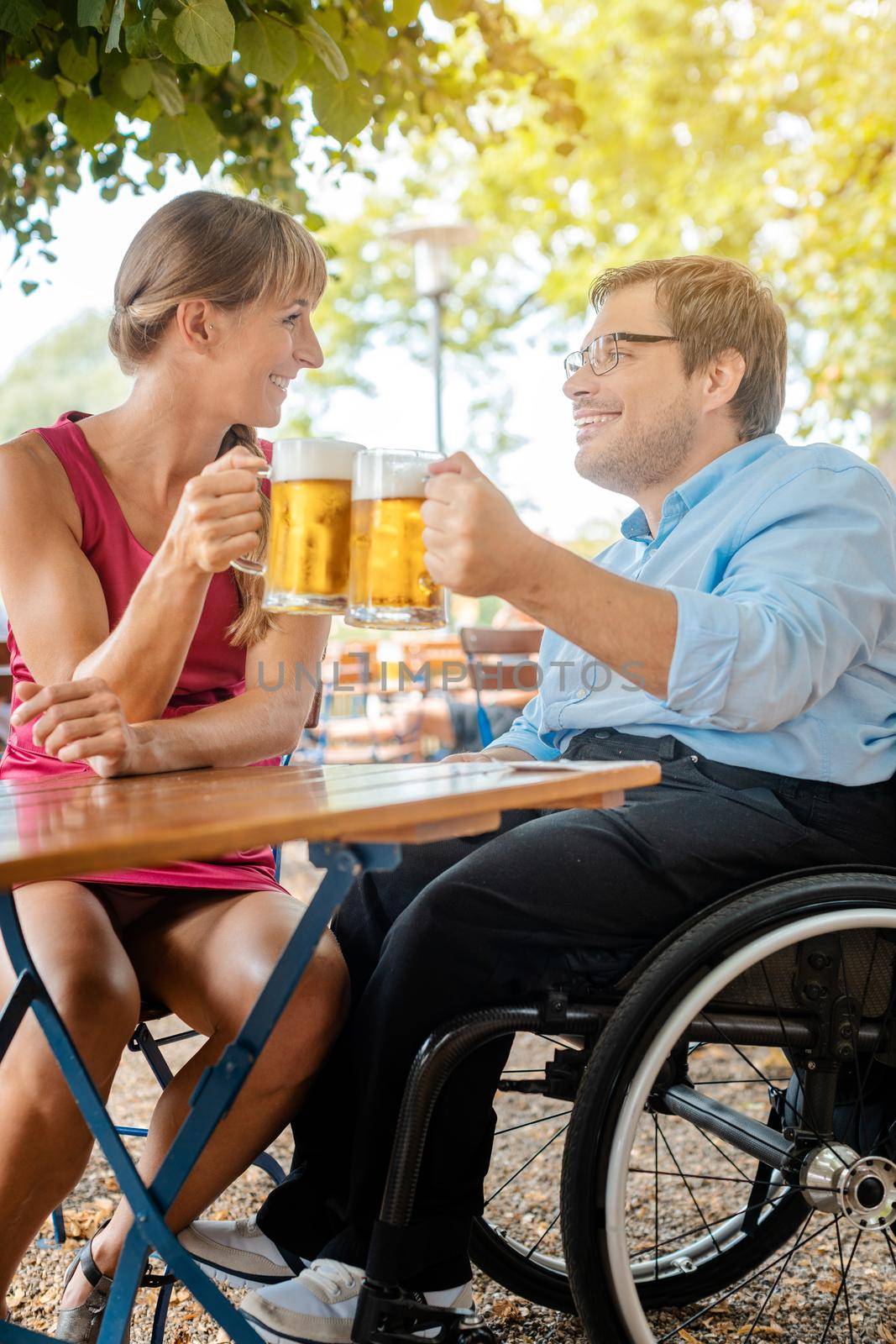 Disabled man in wheelchair and friend drinking beer clinking glasses