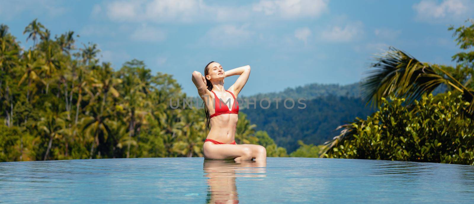 Woman in tropical vacation sitting in the water of pool in front of palm trees
