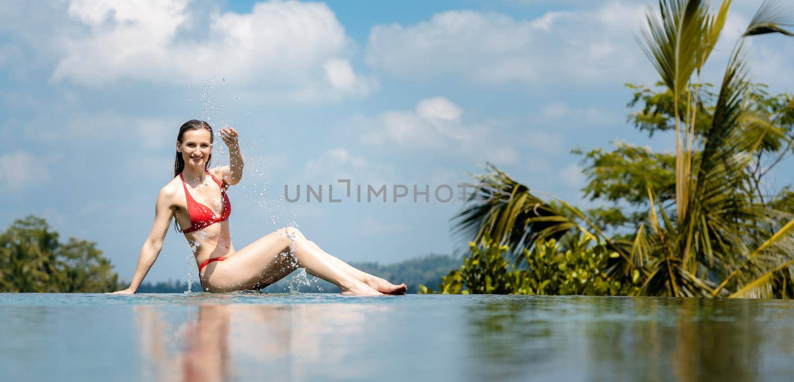 Woman playing with water sitting on edge of the swimming pool
