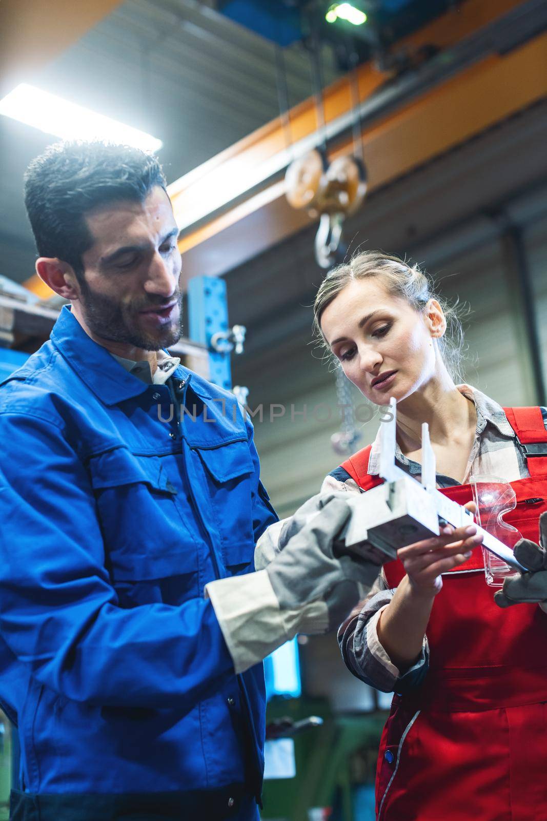Satisfied woman and man worker checking measurements of metal work piece