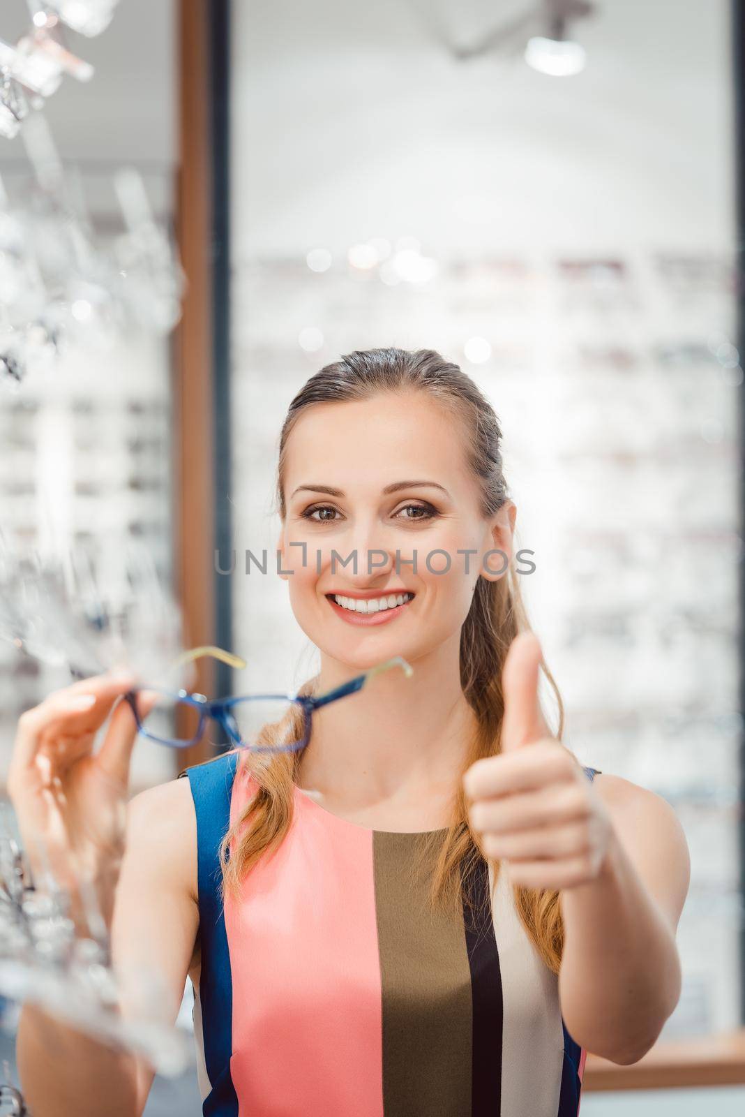 Woman giving thumbs-up for fashionable glasses in optician store by Kzenon