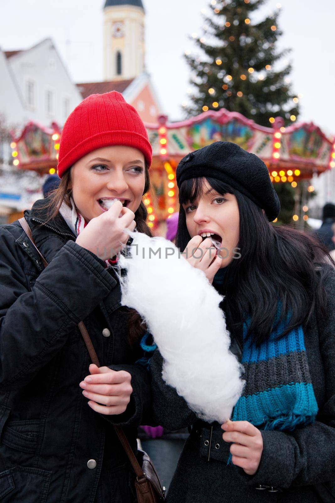 Women on Christmas market eating candy by Kzenon