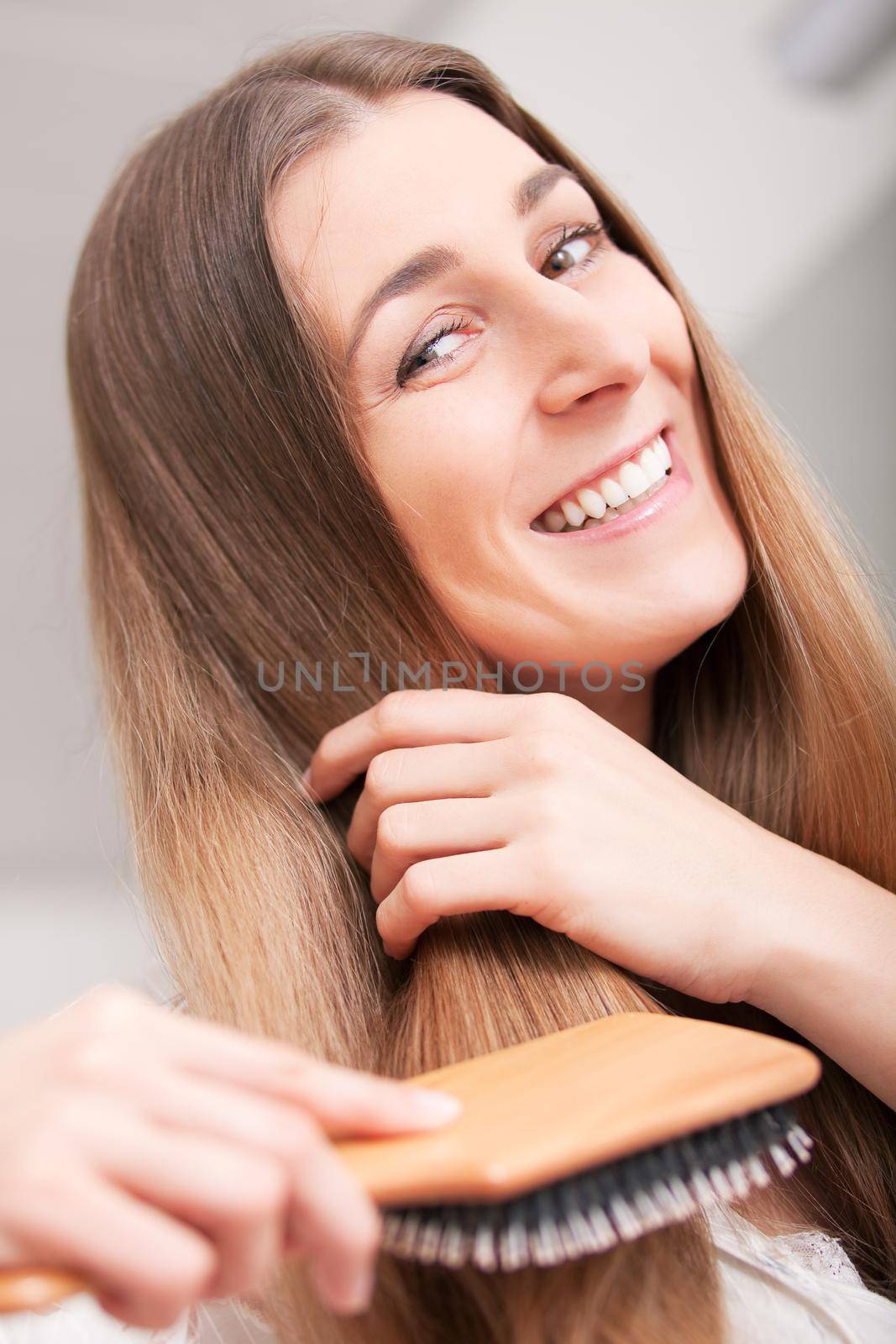 Young woman in pyjama brushing her long dark-blond hair after getting up in the morning