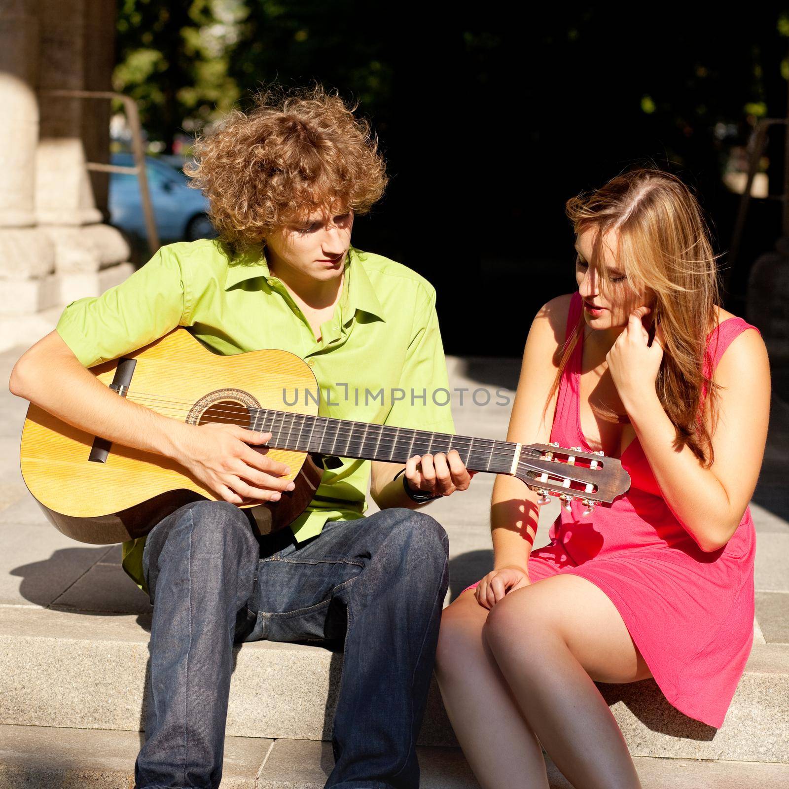 Man and woman in the city - sitting on a wall with guitar