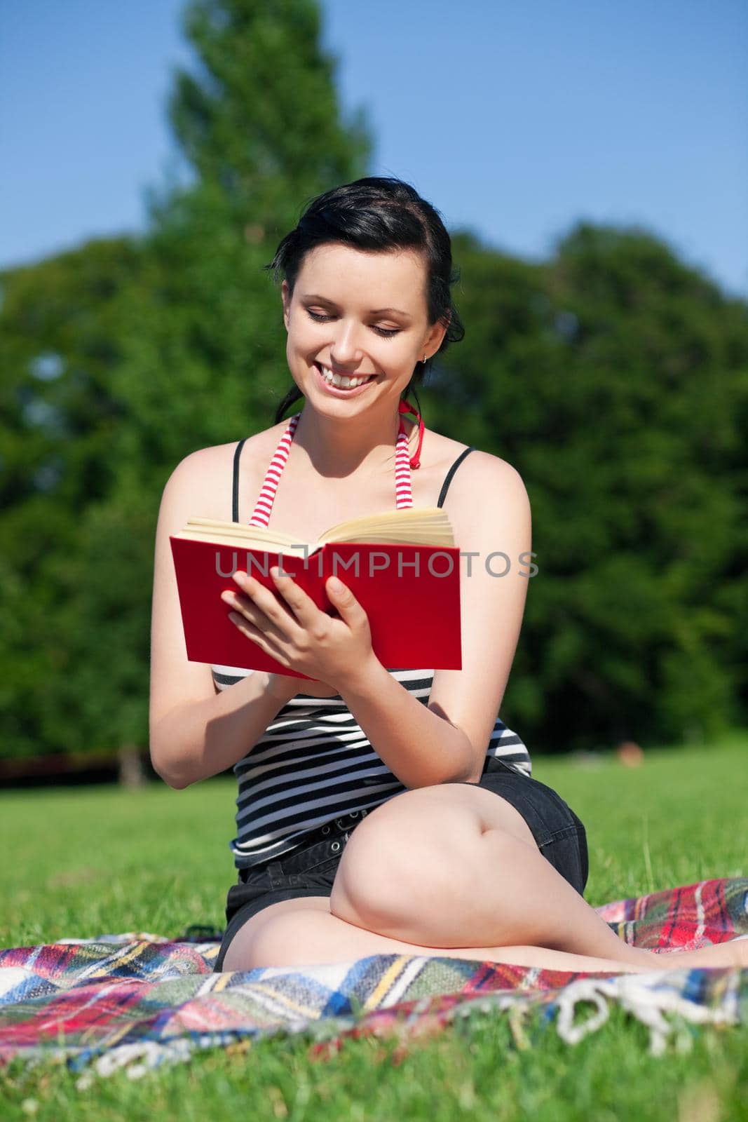 Woman reading book in the sunshine sitting on a meadow in summer