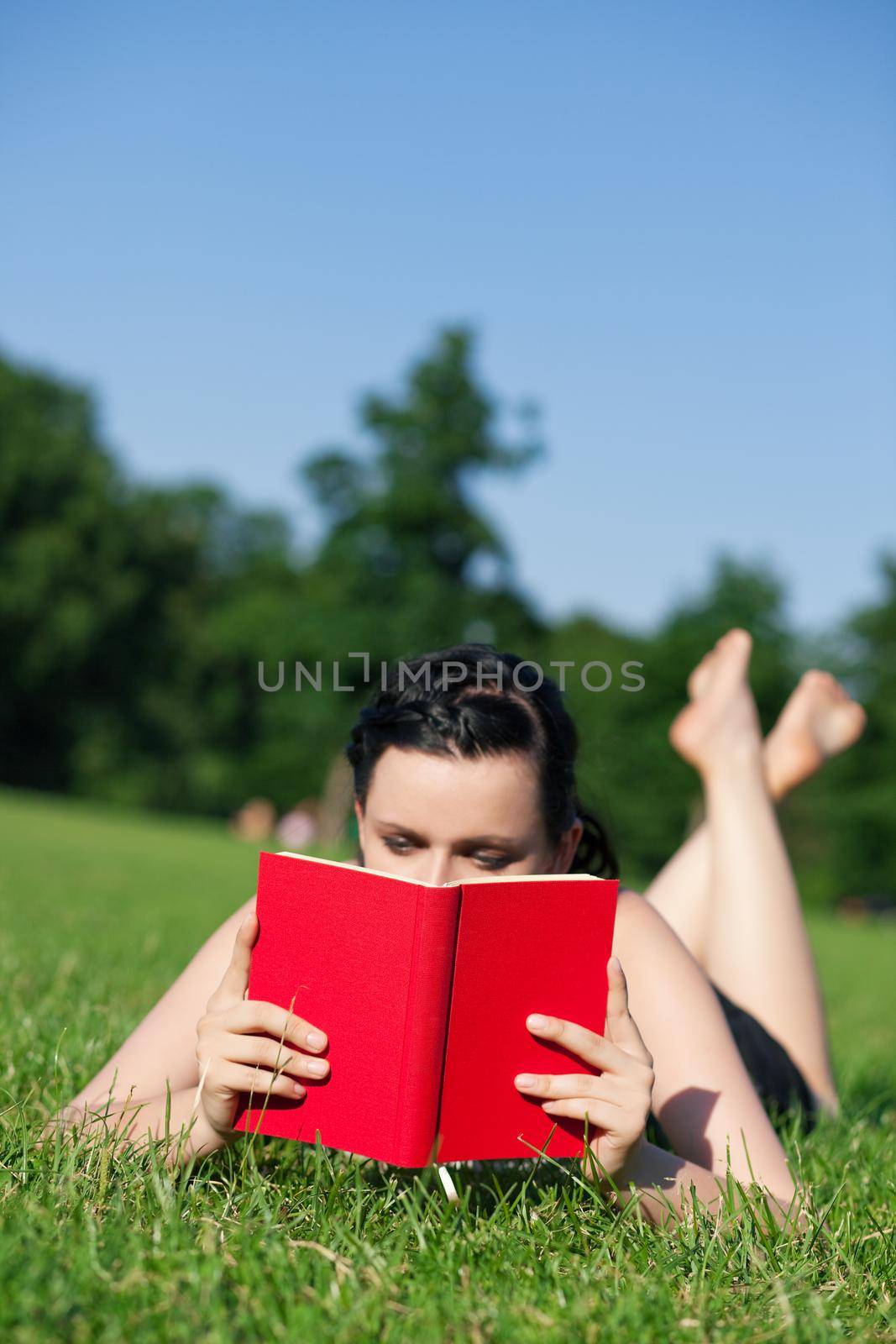 Woman reading book in the sunshine lying on a meadow in summer, FOCUS is on the book