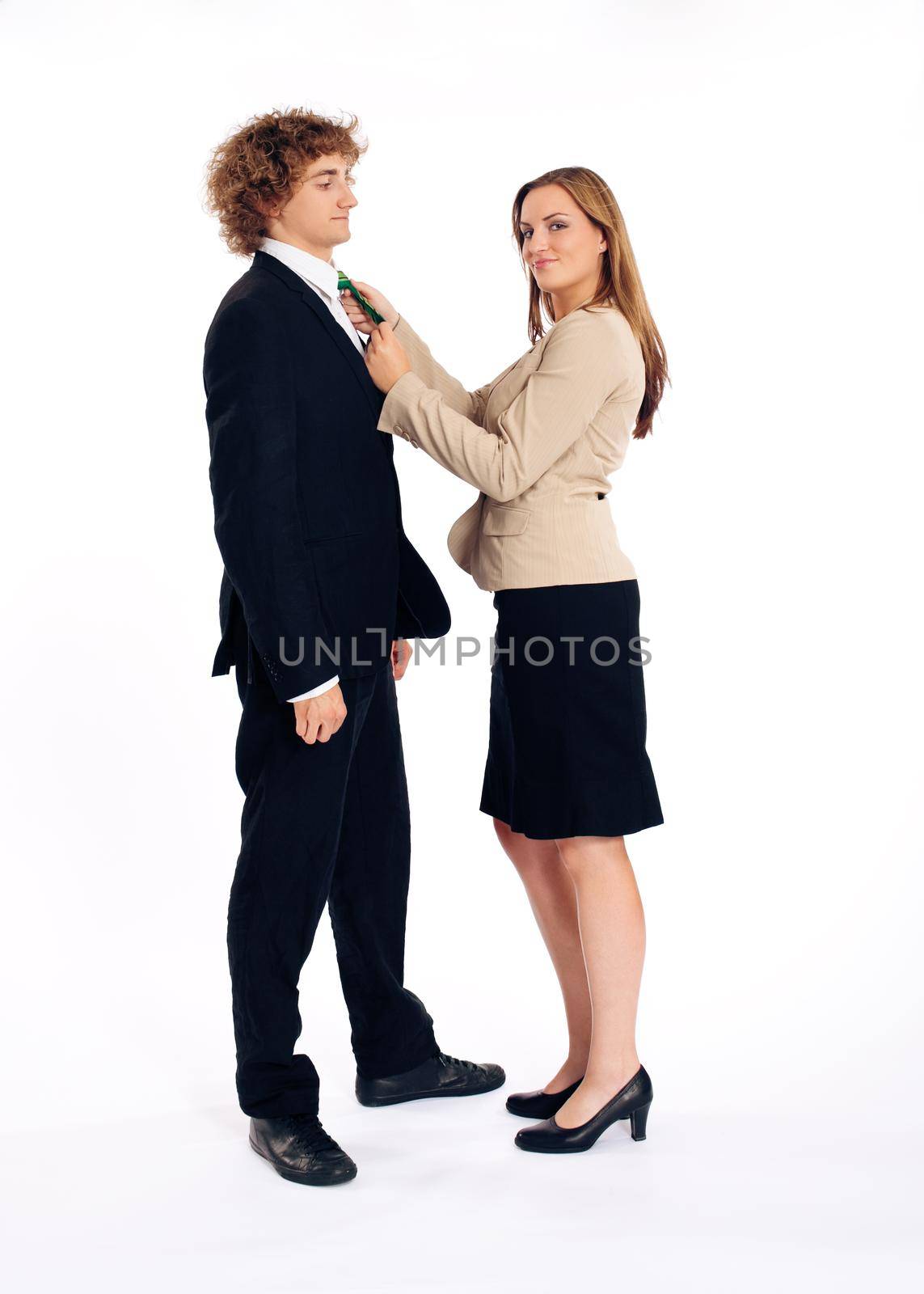 Business people standing in a studio, she is binding his tie