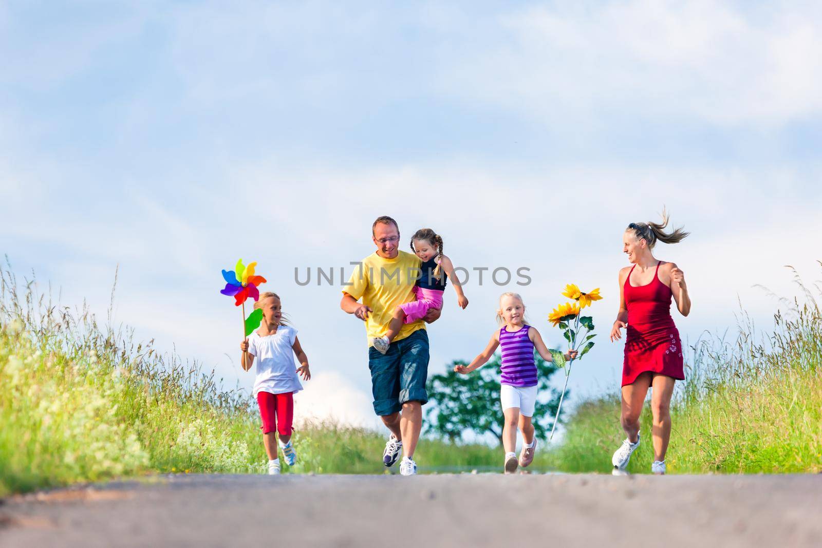 Family running down hill in summer by Kzenon