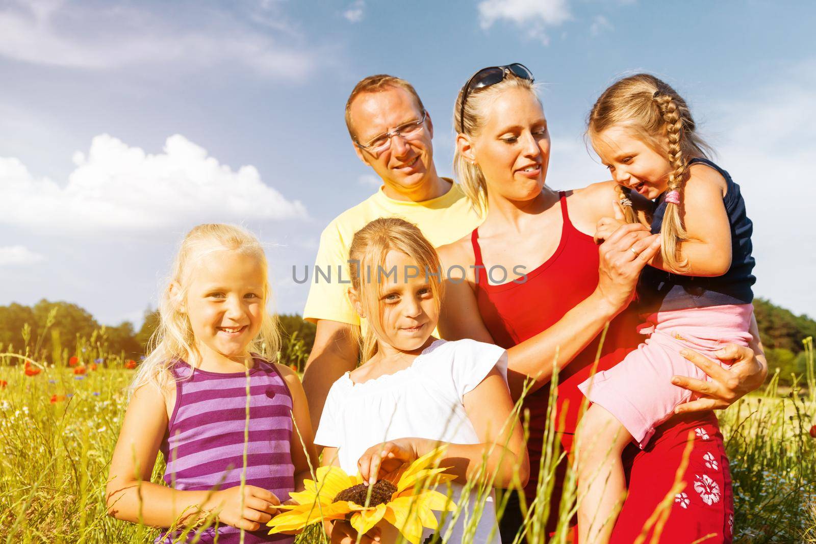 Happy family with tree kids standing in a field of wild flowers together
