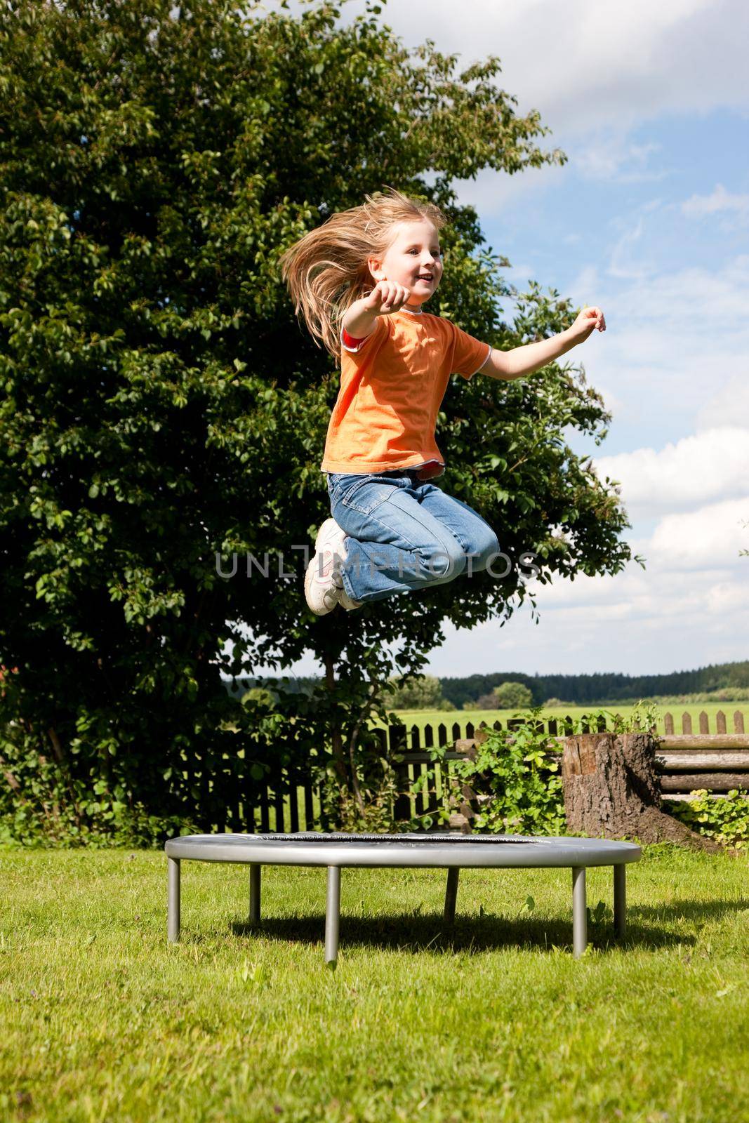 Girl child on trampoline in the garden by Kzenon