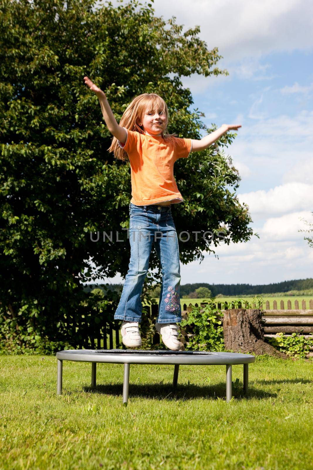 Girl child on trampoline in the garden by Kzenon