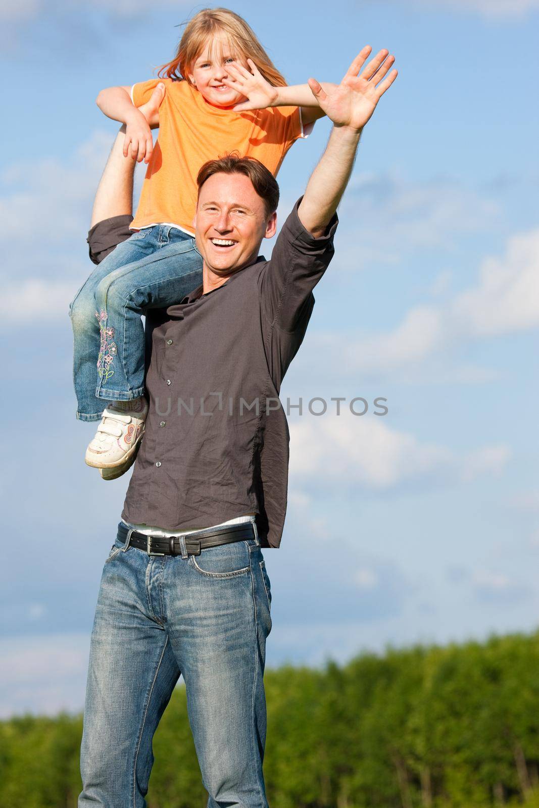 Father and his kid - daughter - playing together at a meadow, he is carrying her on his shoulders