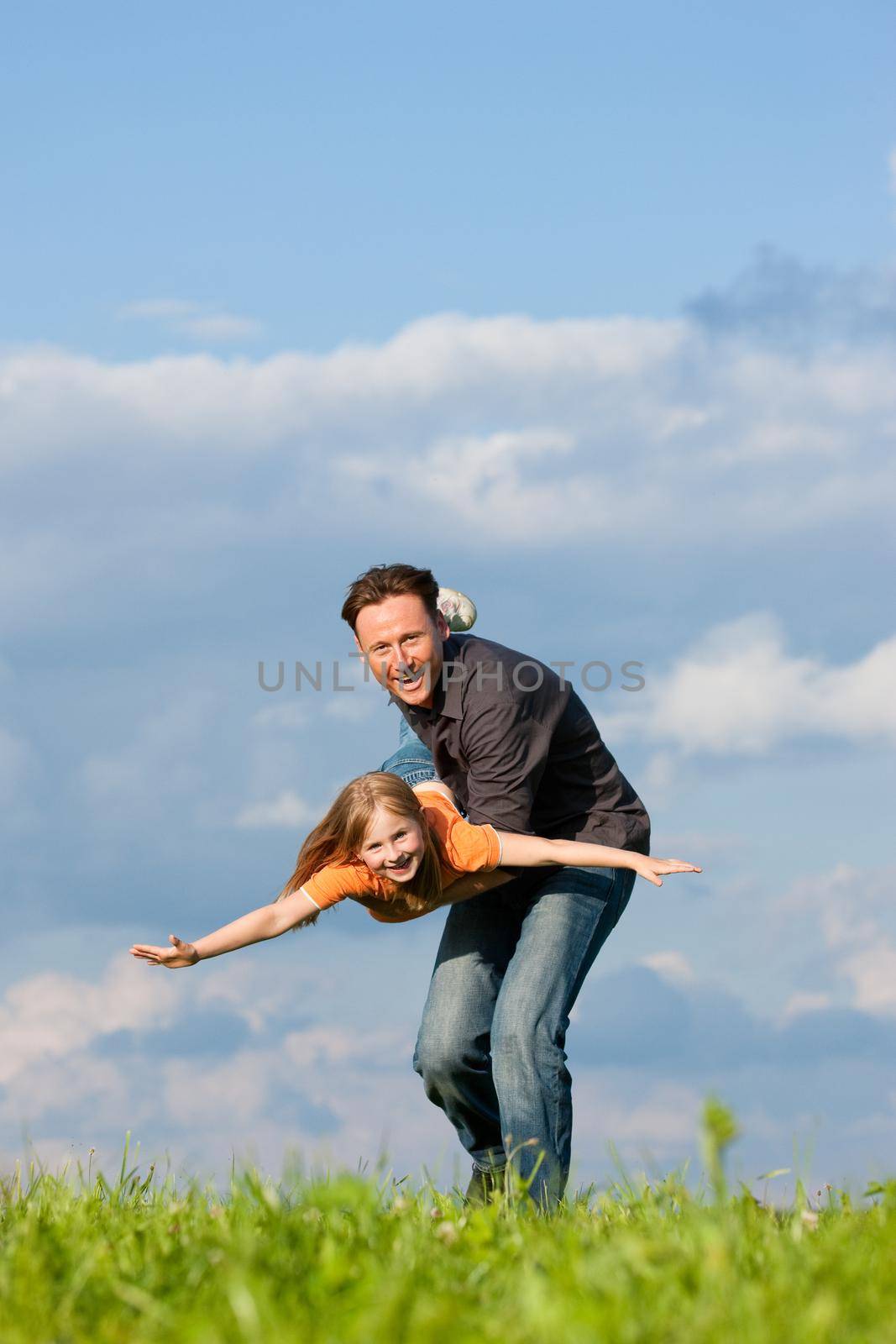 Father and his kid - daughter - playing together at a meadow, he is carrying her on his hands