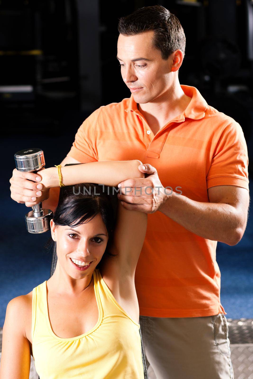 Woman with her personal fitness trainer in the gym exercising with dumbbells