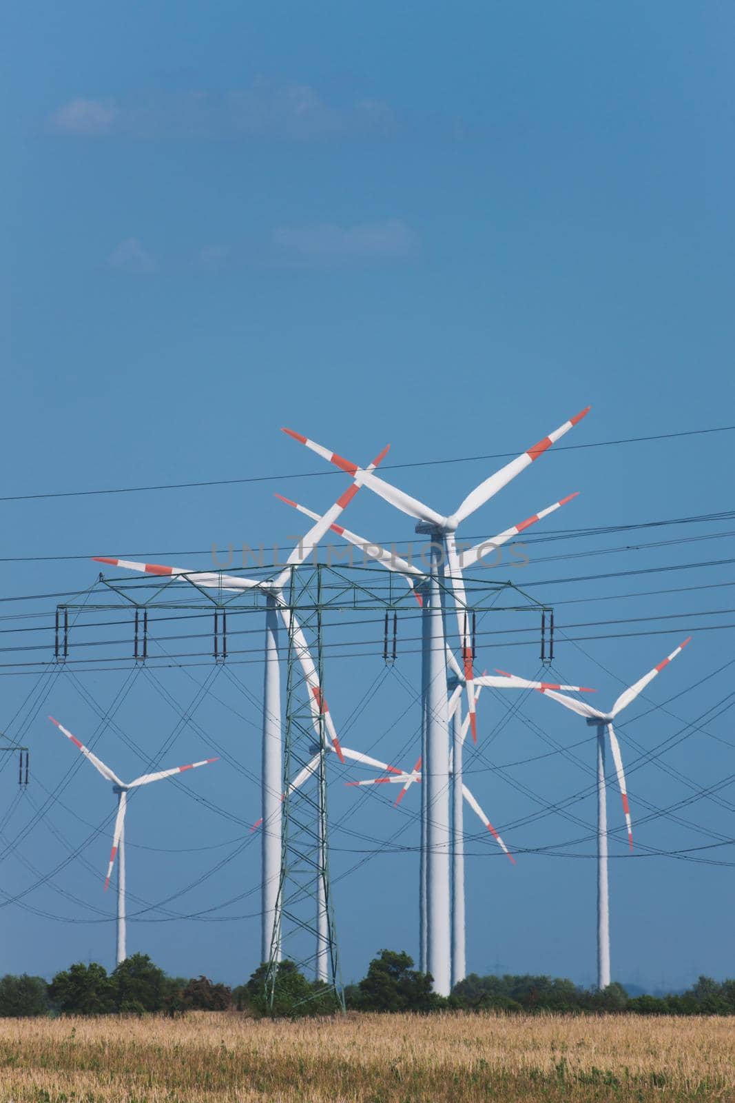 Wind turbines and in the foreground a power transmission line, there is very strong heat haze over the field in the foreground to illustrate the hot summer day