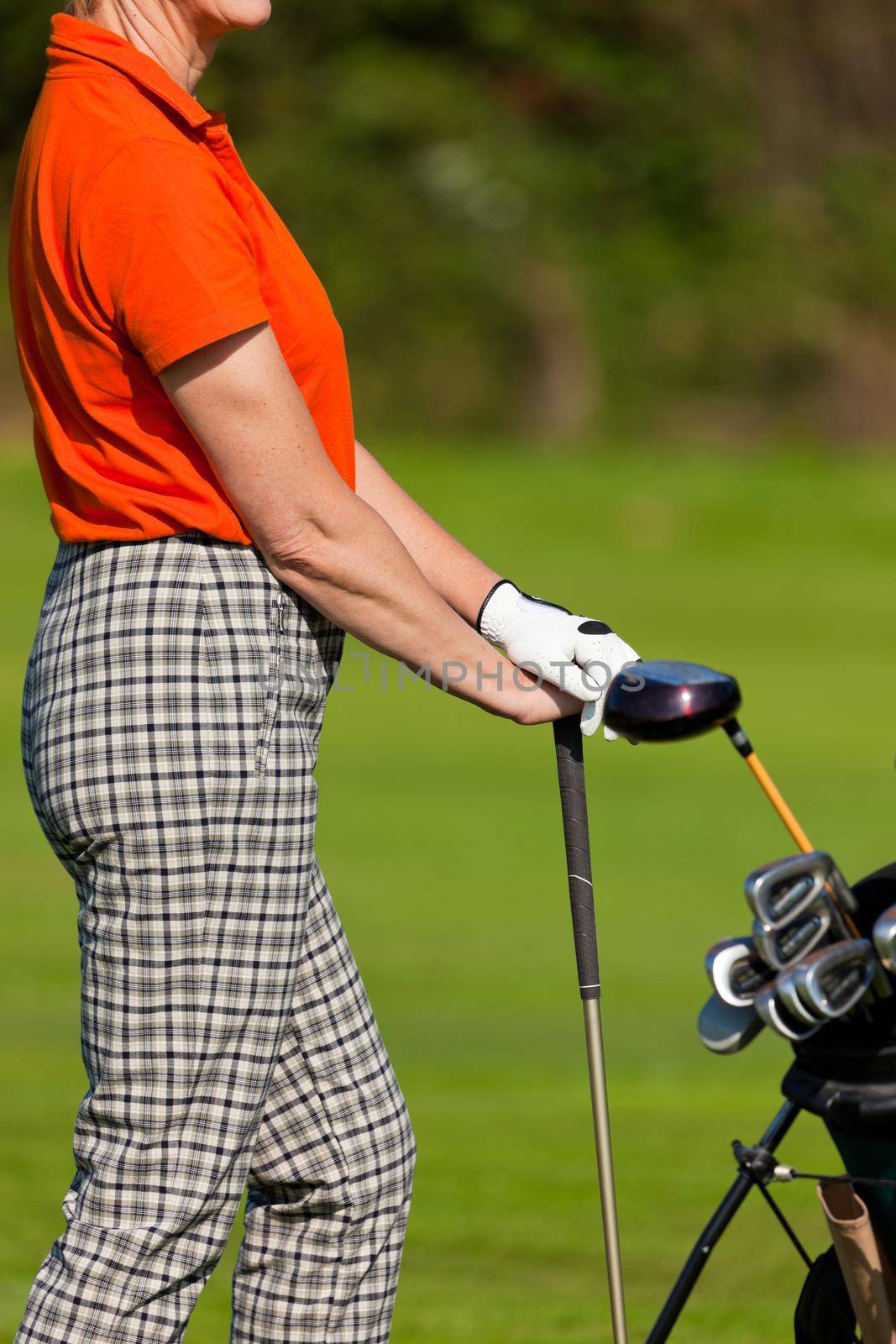 Mature Woman - only torso to be seen - with golf bag playing golf on a golf course