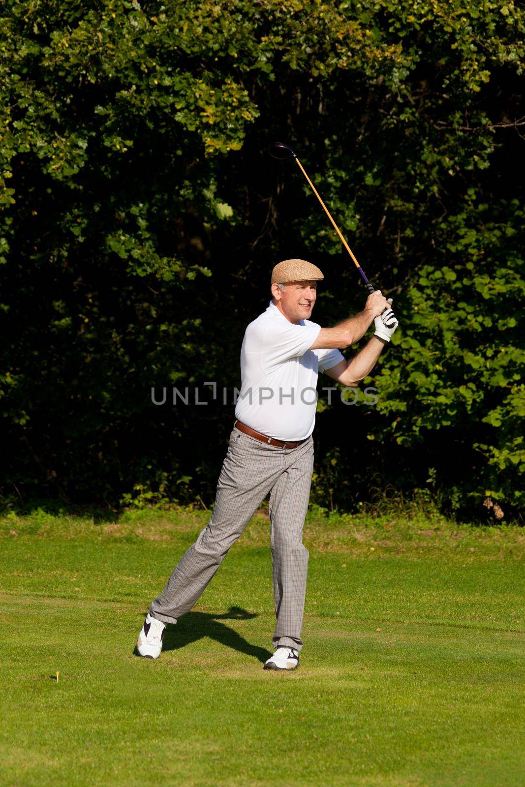 Senior golfer doing a golf stroke, he is playing on a wonderful summer afternoon