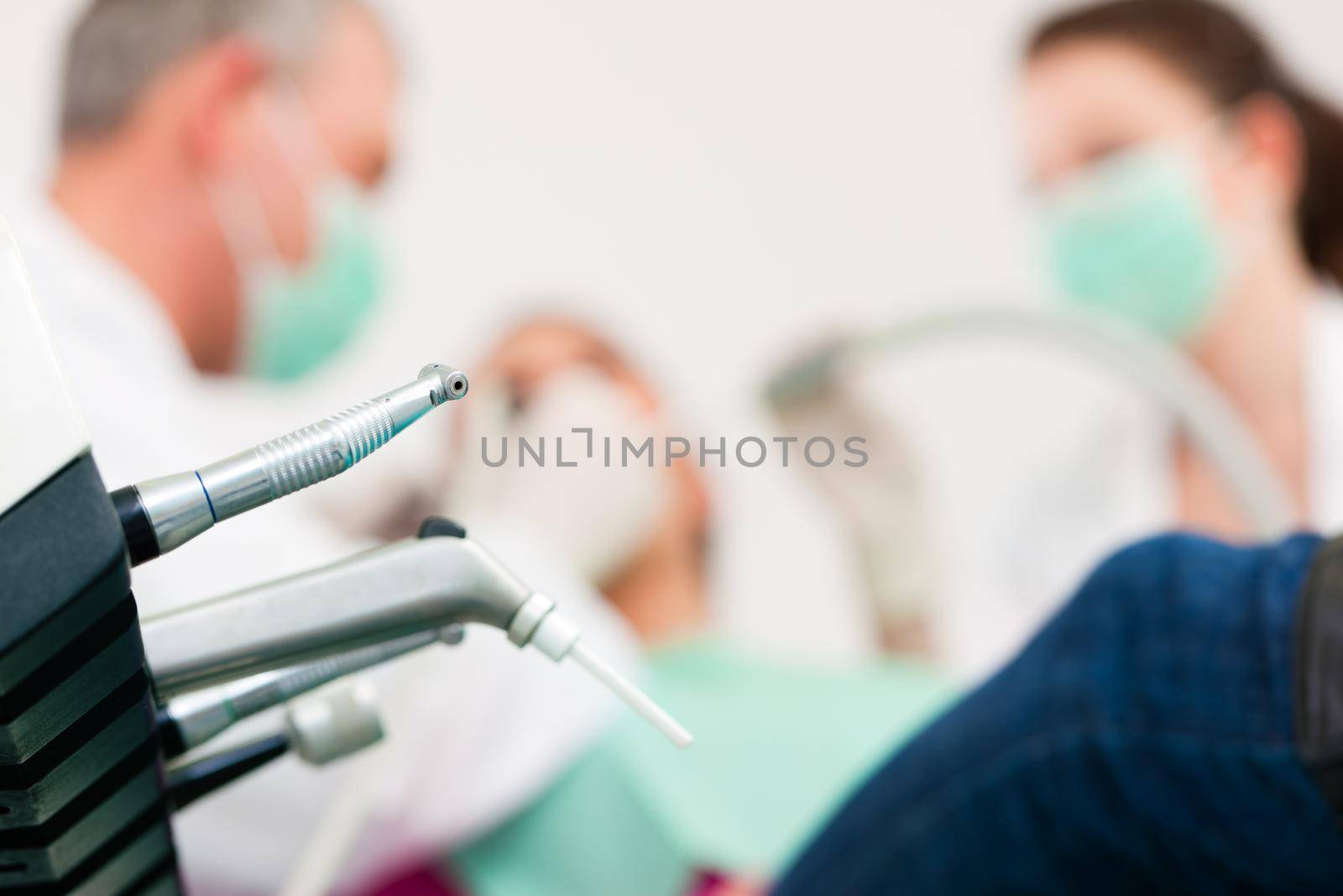 Female patient with dentist and assistant in a dental treatment, wearing masks and gloves, Dentist and assistant bowing over her using sucker and drill