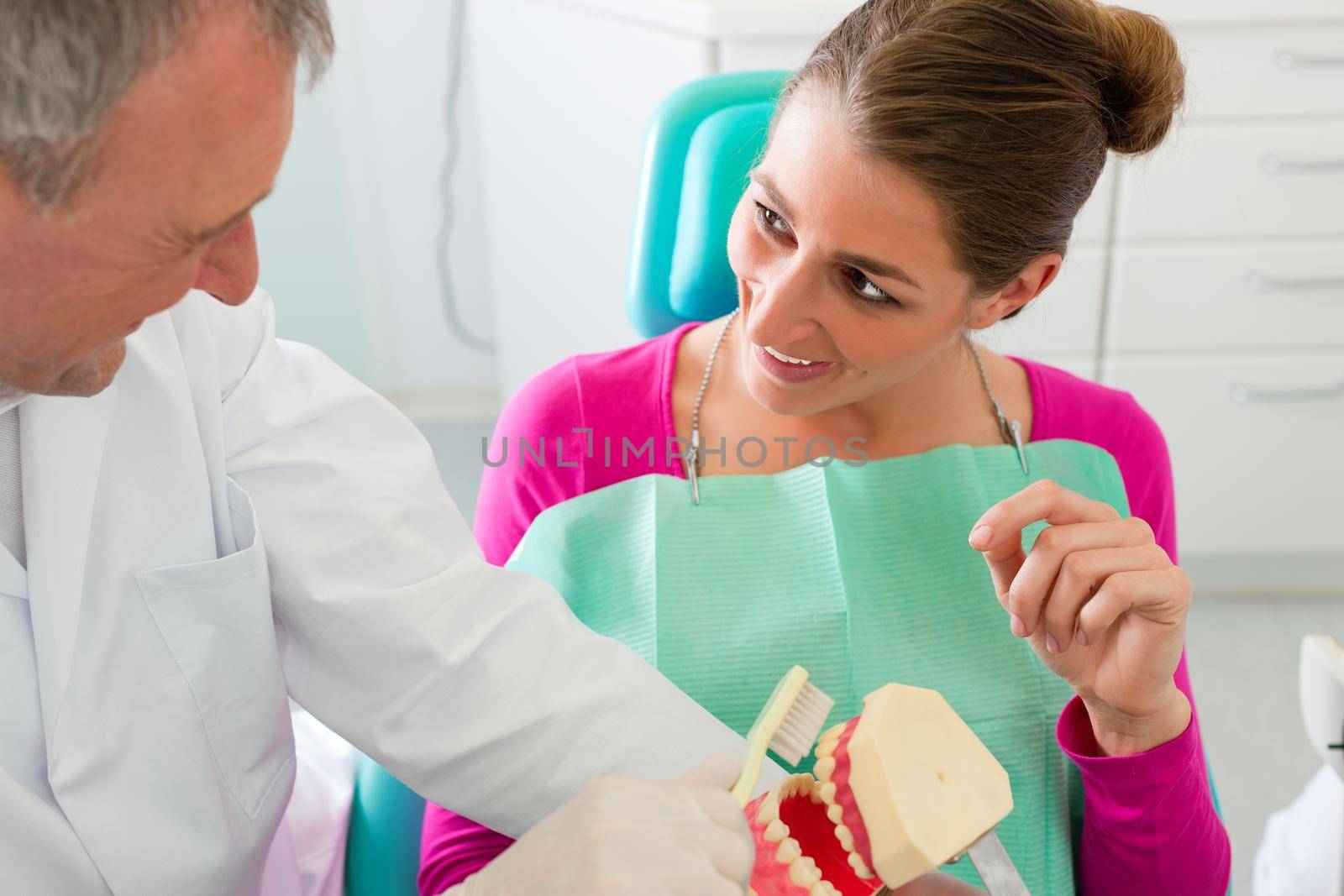 Dentist explaining teeth brushing to patient with an artificial set of teeth