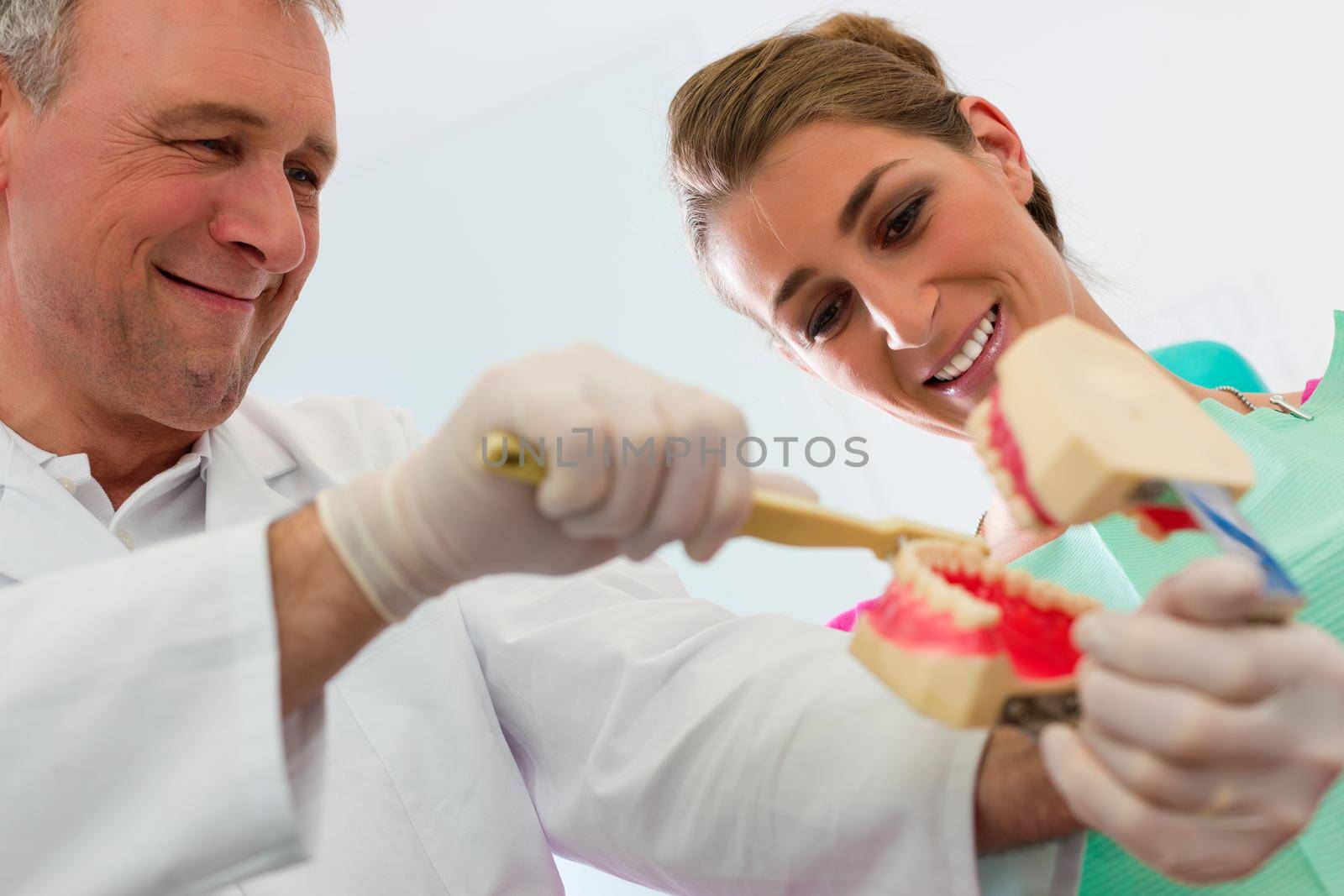 Dentist explaining teeth brushing to patient with an artificial set of teeth