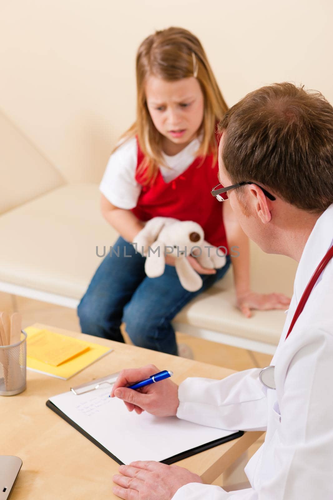 Pediatrician is examining his little patient sitting on a couch and makes some notes